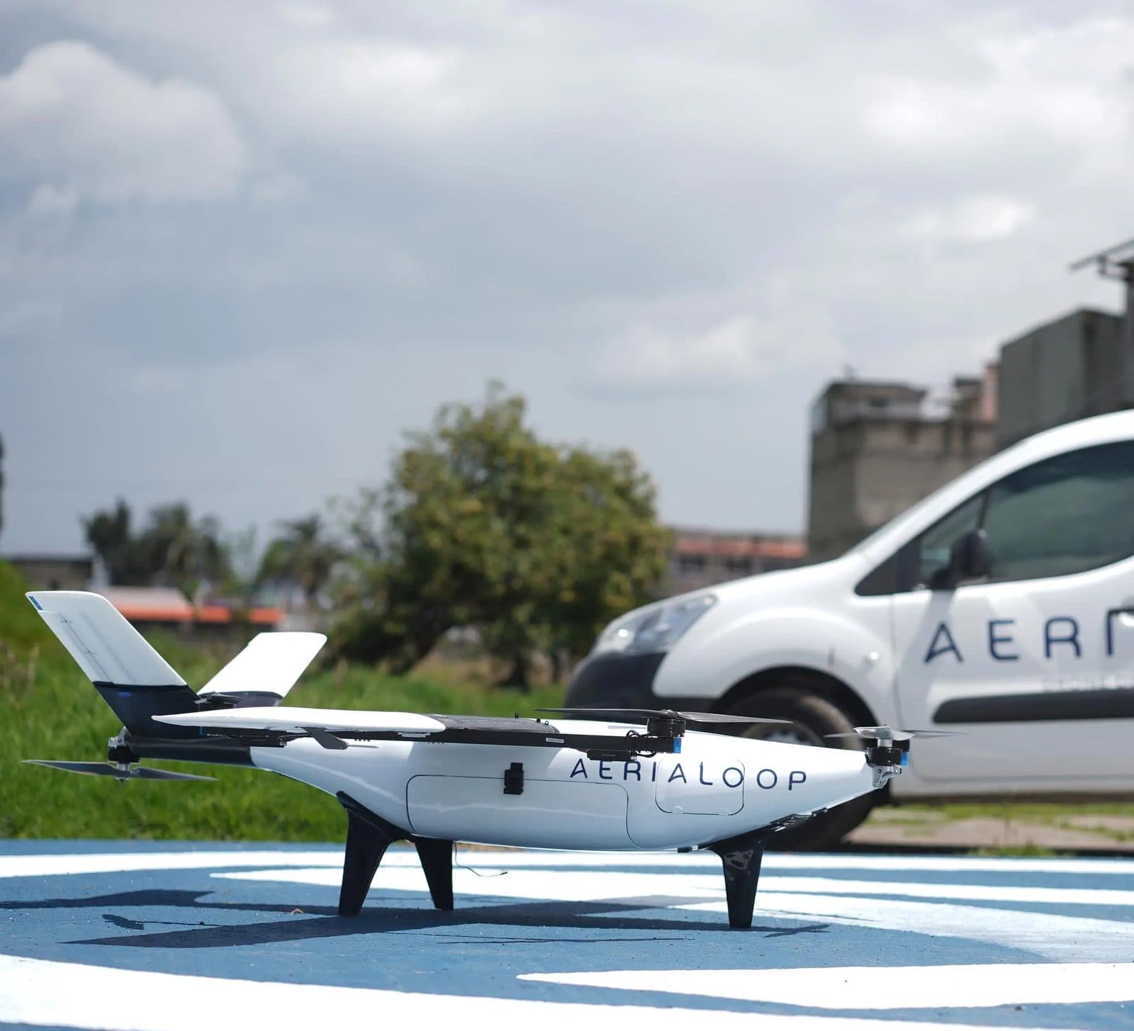 An Aerialoop cargo drone on its landing pad, an Aerialoop van behind it