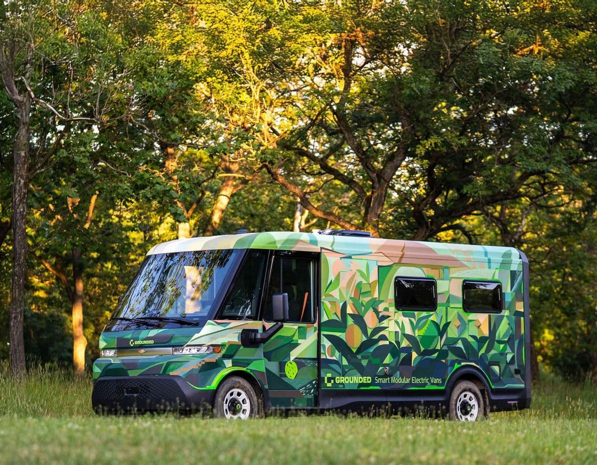 A Grounded electric camper van parked on grass under trees